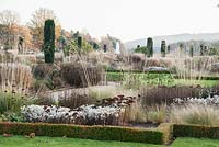 Box edged flowerbeds in the Italian Garden, filled with herbaceous perennials and grasses including Phlomis russeliana, Stipa gigantea, sedums, asters and pennisetum and a row of fastigiate Irish yews, Trentham Gardens