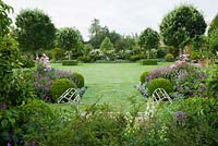 Formal garden with large lawn featuring four Pyrus nivalis underplanted with clipped box and herbaceous borders with pink hardy geraniums, white lychnis and roses 