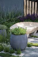 Container planted with sedum, curved oak bench, paving with Thymus argenteus, Rosmarinus officinalis and Lavandula, border planting of Salvia nemorosa and Perovskia - Living Landscapes: Healing Urban Garden, RHS Hampton Court Palace Flower Show 2015