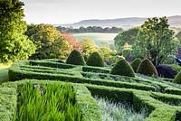 View over the Grasses parterre. Low hedge of Buxus sempervirens, foreground containing Cocosmia 'Lucifer'. Mounds of clipped Taxus baccata. Veddw House Garden, Monmouthshire, South Wales. June 2015. Garden designed and created by Charles Hawes and Anne Wareham.