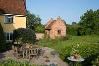 Terrace with wooden table and chairs, terracotta pots. with herbs and hostas. Laurus nobilis - bay tree, Ceanothus and perennials by a newly built brick garden house with crow stepped gables. Heveningham, June