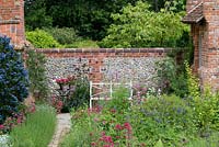 White metal bench, cobble and brick wall with Centranthus Ruber - Valerian,  Ceanothus and terracotta pots with Pelargonium and Petunia. Heveningham, June