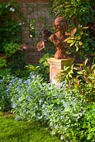Rusty lady sculpture with Brunnera macrophylla 'Jack Frost' - Siberian bugloss 'Jack Frost'. The Court, North Ferriby, Yorkshire, UK. Spring, May 2015.