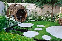 Woven willow bird hide and seating area in bird watcher garden. Chamomile lawn with circular stepping stones and a waterlily pond - Living Landscapes 'City Twitchers', RHS Hampton Court Flower Show 2015 