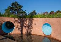 SABO: The Circle of Life Garden - painted rendered wall with water feature, water pouring in to pool lined with stones, planting of Echinacea purpurea 'Eccentric', Tulbaghia cominsii x violacea, Crocosmia 'Lucifer' - Designer Stefano Passerotti - Sponsor Sabo Oil - RHS Hampton Court Flower Show 2015 - awarded Silver Gilt