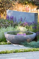 View of concrete circular water feature and grey stone slabs surrounded by Festuca glauca - blue fescue grass, Lavandula, Thyme. Healing Urban Garden, RHS Hampton Court Palace Flower Show 2015