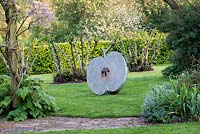 Giant apple sculpture, balanced on lawn in front of 100-year-old Kentish cobnut trees. Sculpture by David Watkinson.