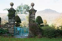 Form of Moel Hebog seen from the forecourt by the entrance to the hosue, framed by topiary yews and decorative gate. Plas Brondanw, Penrhyndeudraeth, Gwynedd, Wales