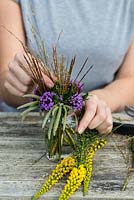 Purple and yellow posie step by step in October: adding stems of purple moor grass alongside Chinese silver grass, silk tassel bush and Verbena bonariensis.
