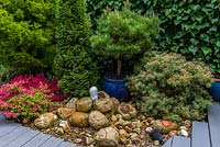 3.7m x 25m contemporary garden. Tucked away beside the path, a white water fountain tumbling down over a bed of sandstone rocks. In blue pot: Pinus thunbergii