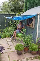Woman reading a book and drinking tea under a blue shaded awning