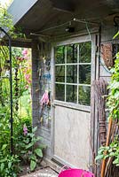 Garden shed entrance with trellis as a holder for gloves and other garden tools, next to the door, a broom, Digitalis purpurea