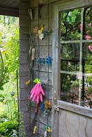 Garden shed entrance with rubber gloves and garden tools suspended on a trellis