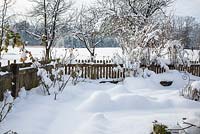Winter in a farmer's garden with wooden picket fence and an orchard