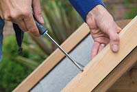 Using a screwdriver  to attach the wooden batons to the outer rim of the kennel roof