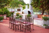 Patio with red floor, metal table and chairs, built in outdoor kitchen with barbeque and pizza oven.  Alaior, Menorca. 