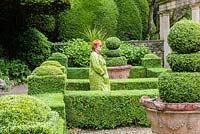 Visitor in the Formal garden next to the Great Terrace colonnade and Casita. Hedges and topiary of Buxus sempervirens. Clipped Yew behind. Terracota pot from Italy.Iford manor, Bradford-on-Avon, Wiltshire. July. Garden designed and created by Harold Peto. Historic garden grade I.