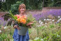 Sheree King holding a bucket of Lupins, Panicum violaceum, Dahlias and Panicum elegans 'Frosted Explosion'