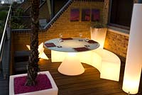 Contemporary balcony overlooking the Thames at Wapping with illuminated dining plastic dining furniture and a cordyline in a container 