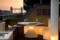 Contemporary balcony overlooking the Thames at Wapping dusk evening with illuminated white plastic dining furniture in small space  Wapping Balcony
