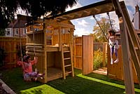 Girls on swings in a small urban contemporary town garden. Play area with wooden climbing frame. Ansari garden, Harrow