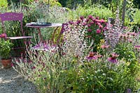 Small sitting area on gravel terrace. Cottage garden planting with Salvia sclarea - clary sage, Echinacea purpurea - purple coneflower, Silene syn. Lychnis coronaria and Monarda in the flowerbed