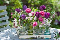 Cut spring flowers in jars and bottles in Tulipa, Ranunculus - buttercups and branches of Malus 'Evereste' 