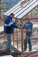 Installing and setting up a greenhouse. Two Men putting glass panels into the wooden frame