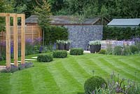 Path leading from pergola to the sunken seating area, with potted Astelia chathamica, Buxus sempervirens cubes and Verbena bonariensis