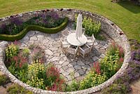 View from above of sunken terraced area with garden furniture table chairs and planting of Phlomis Salvia Penstemon and Geranium, Follers Manor, Sussex 