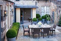 Outdoor contemporary space featuring set table on cobble floor, box ball topiary in containers and Acer Japonica 'Aconitifolium'