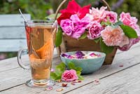 A glass of Rose tea with a trug of cut Roses and petals