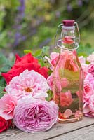 Rose water in a glass vase surrounded by cut roses