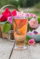 A glass of rose tea with a trug of cut roses and petals