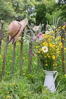 A jug of wildflowers against a rustic fence, with a view to a meadow of Buttercups - Ranunculus