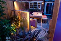 Contemporary long narrow small urban garden with dining table and low maintenance planting 