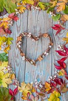 A colourful border of mixed autumnal leaves with a woven wreath, spent hydrangea flowers and blossom