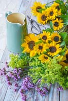 A green ceramic jug with fresh cut sunflowers, alchemilla mollis and verbena bonariensis
