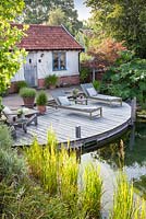 Tranquil summer scene with swimming pond, recliners and decking.