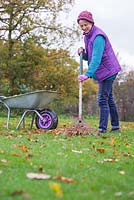 A woman raking the garden lawn of fallen autumnal leaves