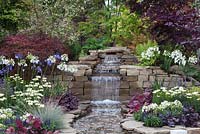 The waterfall in the centre of 'The Water Garden' at RHS Tatton Flower Show 2015, bordered by dense, colourful planting 