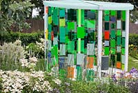 Pavillion made of light reflecting fibre optic panels framed with dense planting in 'Reflecting Photonics' Garden at RHS Tatton Flower Show