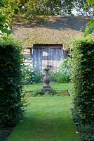 A gap in a beech hedge provides a view from the Lime Allee into the Sundial Garden at Wollerton Old Hall Garden, Shropshire. Planted against the shed are white roses, Centranthus ruber 'Albus', Violas and Geraniums. July.