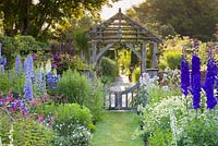 Early morning in the Sundial Garden at Wollerton Old Hall Garden, Shropshire - photographed in July. Planting includes Delphiniums, Salvia microphylla, Knautias, Verbascums, Clematis 'Warsaw Nike' and Geraniums. The oak gate was designed in Arts and Crafts style