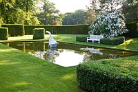 A contemporary Japanese pond garden. Cubes of Hedera - Ivy. White marble sculpture 'Hokusai's boat' by Jessica Walters. Designer Georgia Langton. Farleigh House, Hampshire.