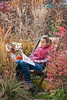 Woman relaxing on a deck chair reading garden magazine in autumn garden.