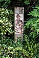 Painted ceramic tiles with a fern pattern on a wooden post in a shady corner.