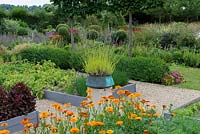 A potager with raised beds of vegetables and flowers. A stone plith with a copper pot planted with lavender provides a central focal point.
