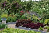 A potager with raised beds of vegetables and flowers including chives, salad leaves, peas, marigolds, cephalarea, lady's mantle and bergamot.
