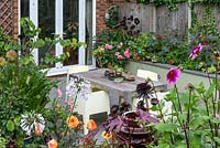 A patio seating area with contemporary garden furniture surrounded by colourful raised borders with dahlia, ahapanthus, ricinus, aeonium and katsura.